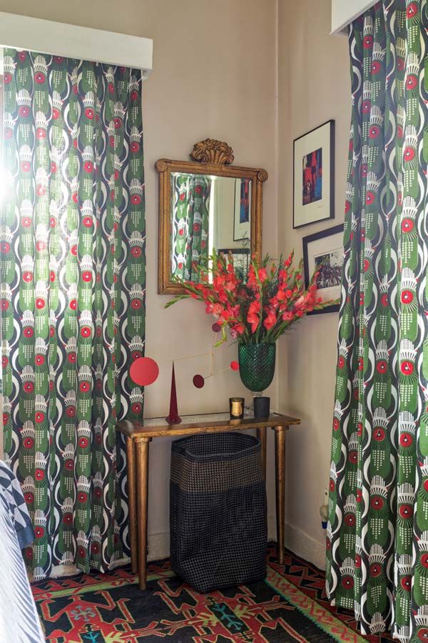 A bedroom corner with green curtains and a table with a golden framed mirror above it